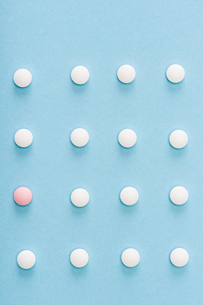 Flat lay with pink pill among white on blue background - Photo, Image
