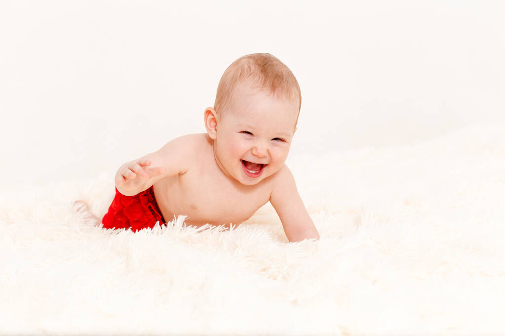 een blanke vrolijke baby kruipt op het bed op een pluizige deken thuis. een kind jonger dan één jaar. Acht maanden. alleen in slipje - Foto, afbeelding