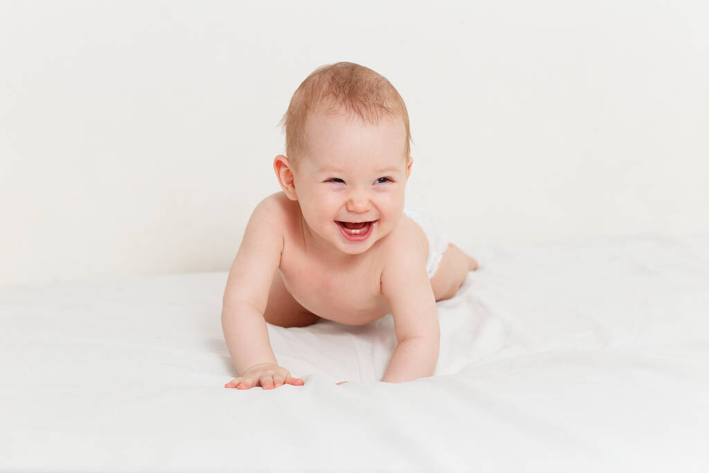 8 aylık gülümseyen bir bebek beyaz bir çarşafın üzerinde emekliyor. Komik çocuk. - Fotoğraf, Görsel
