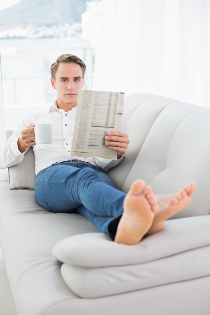 Relajado hombre bebiendo café mientras lee el periódico en el sofá
 - Foto, Imagen