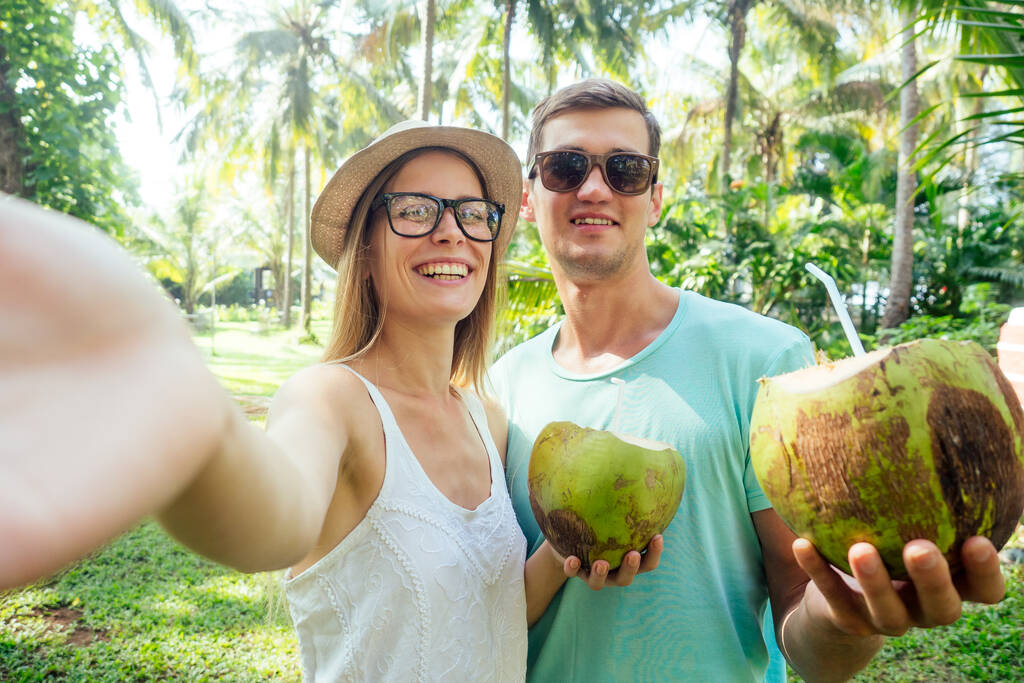 Молодая любящая пара пьет кокос, делая селфи фотографии на камере смартфона
 - Фото, изображение