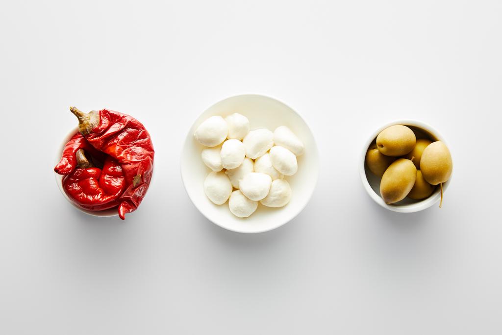Top view of bowls with olives, marinated chili peppers and mozzarella on white background  - Photo, Image