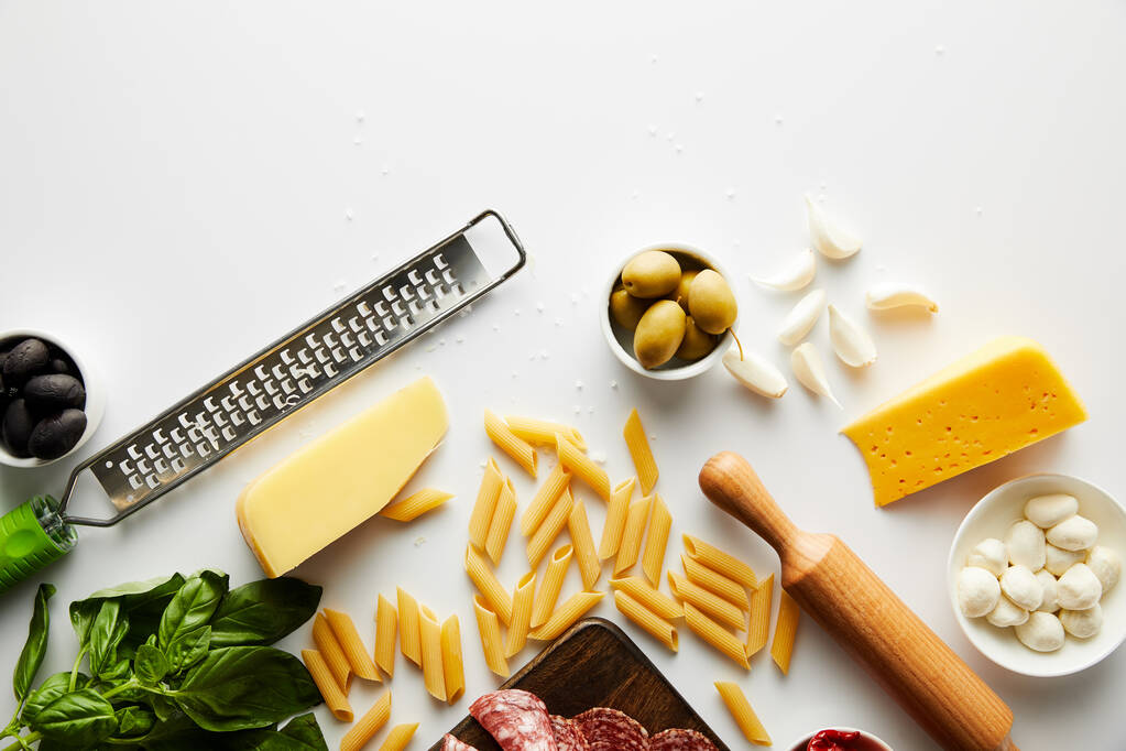 Bovenaanzicht van rasp, deegroller, pasta en ingrediënten op witte achtergrond  - Foto, afbeelding