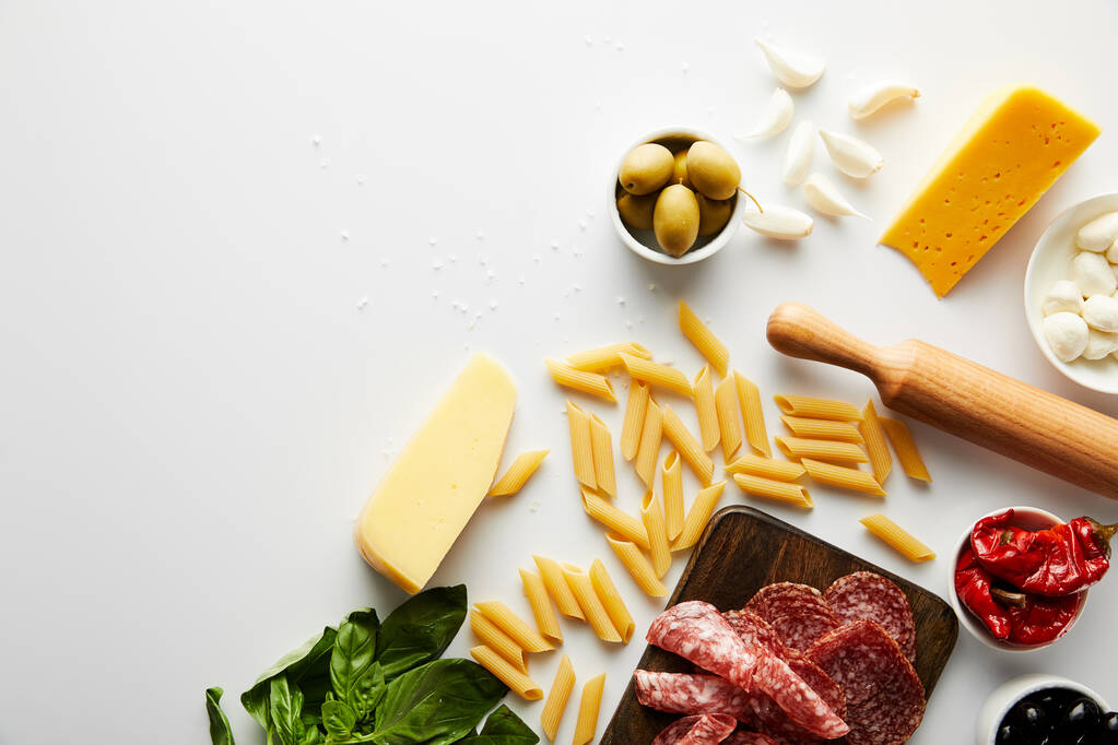 Bovenaanzicht van vleesschotel, deegroller, pasta en ingrediënten op witte achtergrond  - Foto, afbeelding
