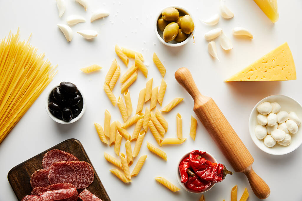 Top view of meat platter, rolling pin, pasta and ingredients on white background  - Photo, Image