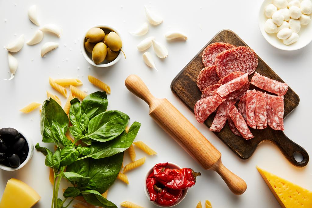 Vista dall'alto di piatto di carne, mattarello, foglie di basilico e ingredienti su sfondo bianco
  - Foto, immagini