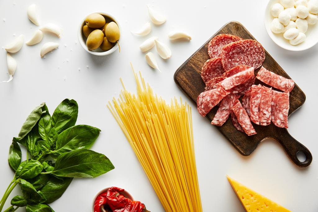 Vista superior de espaguetis, bandeja de carne, hojas de albahaca e ingredientes sobre fondo blanco
  - Foto, Imagen