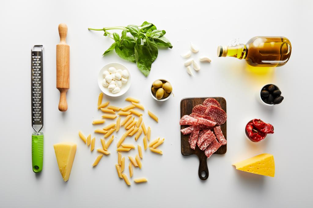 Flache Lage mit Fleischplatte, Flasche Olivenöl, Nudelholz, Reibe und Zutaten auf weißem Hintergrund  - Foto, Bild