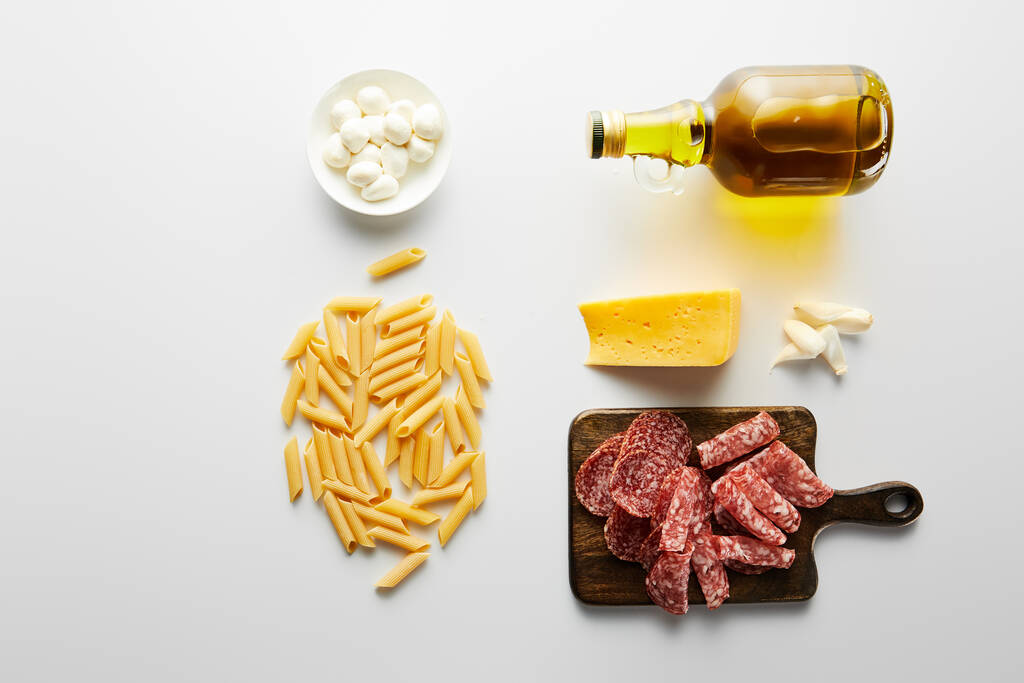 Flache Lage mit Fleischplatte, Flasche Olivenöl, Knoblauch, Käse, Nudeln und Schüssel mit Mozzarella auf weiß  - Foto, Bild