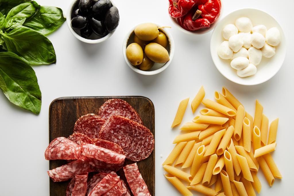 Widok z góry talerz mięsa, makaron, liście bazylii i miski ze składnikami na białym tle  - Zdjęcie, obraz