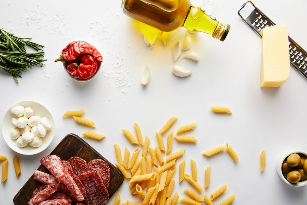 Vue du dessus de la bouteille d'huile d'olive, plateau de viande, râpe, pâtes et ingrédients sur fond blanc
  - Photo, image