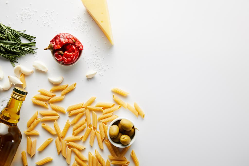 Bovenaanzicht van fles olijfolie, pasta, kaas en ingrediënten op witte achtergrond  - Foto, afbeelding