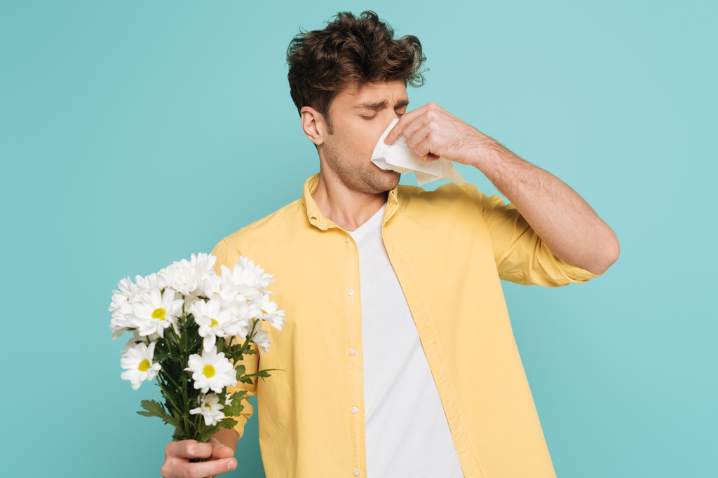 Man blowing out nose with napkin and holding bouquet with outstretched hand isolated on blue - Photo, Image