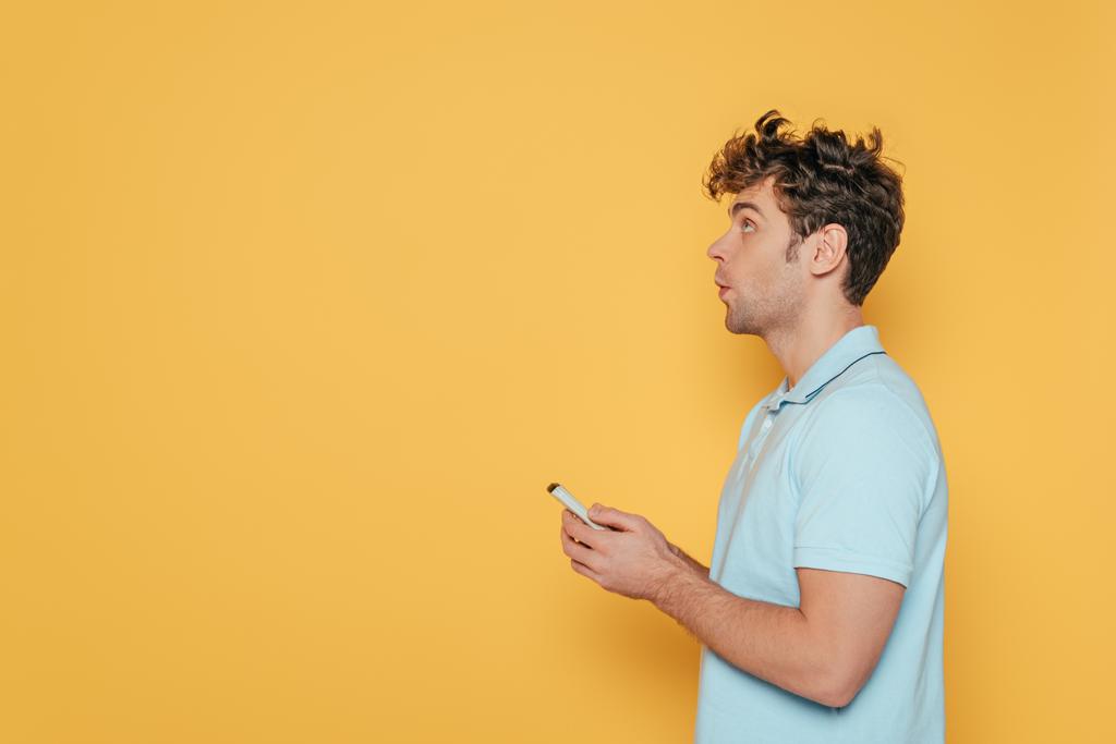 Vista lateral del hombre sosteniendo mando a distancia aislado en amarillo
 - Foto, Imagen