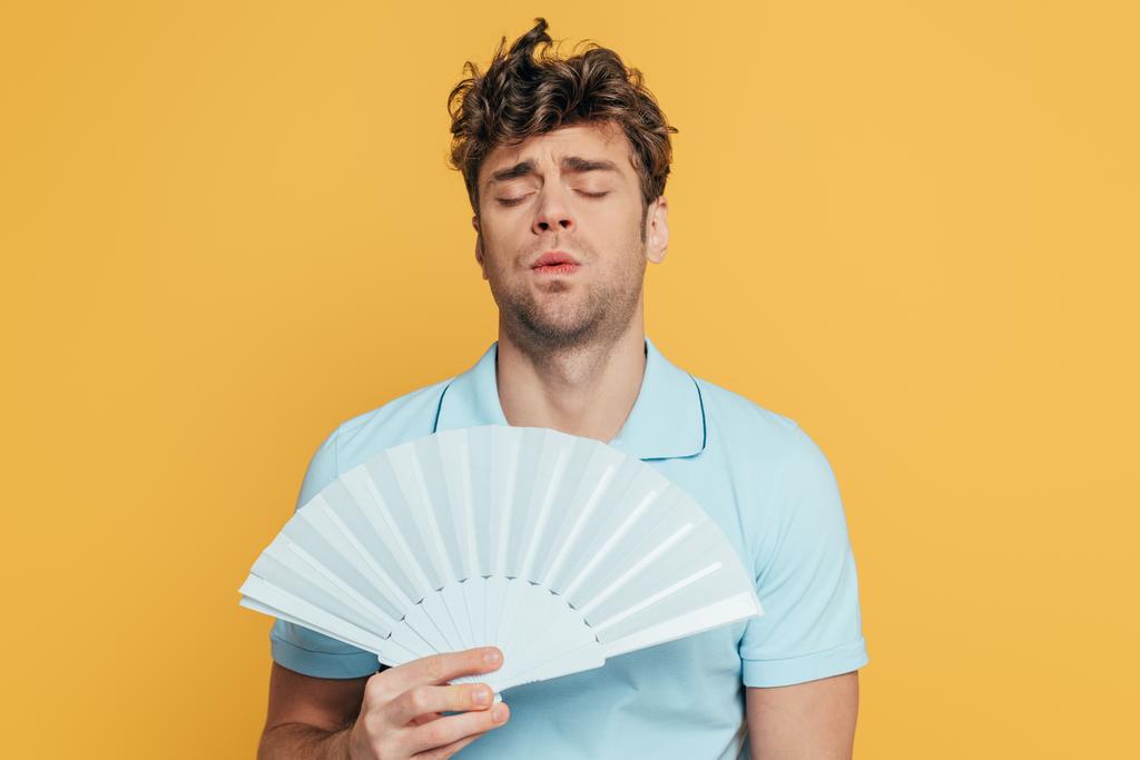 Mann mit geschlossenen Augen und Handventilator leidet unter Hitze isoliert auf gelb - Foto, Bild