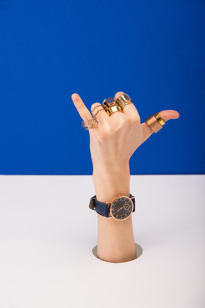 cropped view of woman with wristwatch and golden rings showing call me gesture isolated on blue - Photo, Image