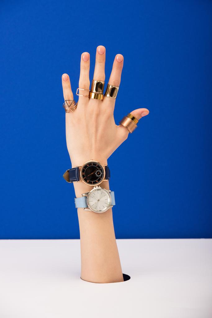 abgeschnittene Ansicht einer Frau mit Armbanduhren und goldenen Ringen isoliert auf blau - Foto, Bild