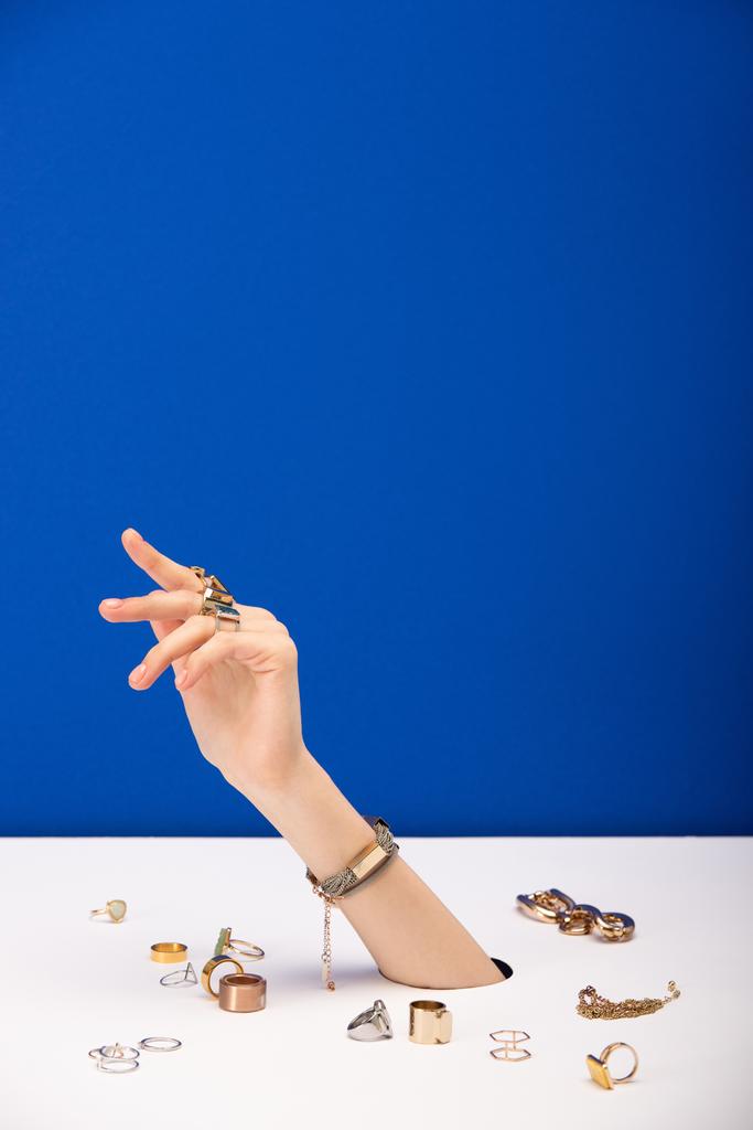 обрезанный вид женщины с браслетом на руке рядом золотые кольца изолированы на синий
 - Фото, изображение