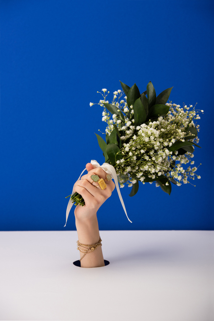 καλλιεργημένη άποψη της γυναίκας με βραχιόλι κρατώντας μπουκέτο από μικρά ανοιξιάτικα λουλούδια απομονώνονται σε μπλε - Φωτογραφία, εικόνα