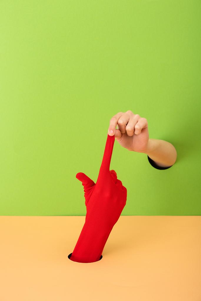 oříznutý pohled na ženu svlékající si červenou rukavici na oranžové a zelené - Fotografie, Obrázek