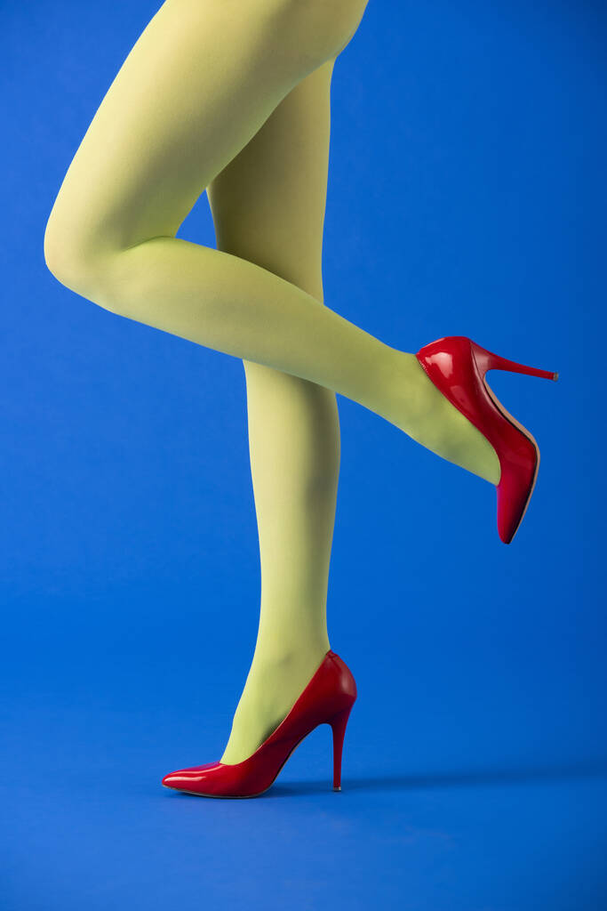 vista ritagliata del modello alla moda in calzamaglia verde e tacchi in posa su blu
  - Foto, immagini