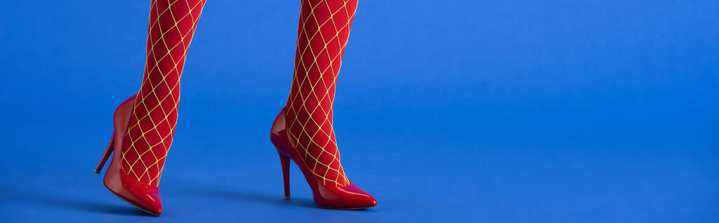 tiro panorâmico de mulher em meias meia-calça e saltos vermelhos posando em azul
  - Foto, Imagem