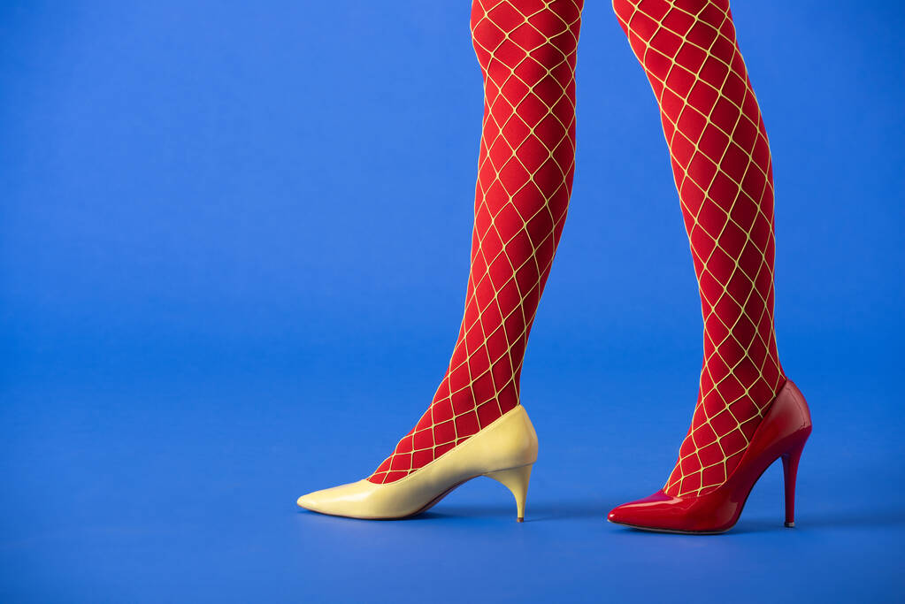 cropped view of woman in fishnet tights, yellow and red heels standing on blue - Photo, Image