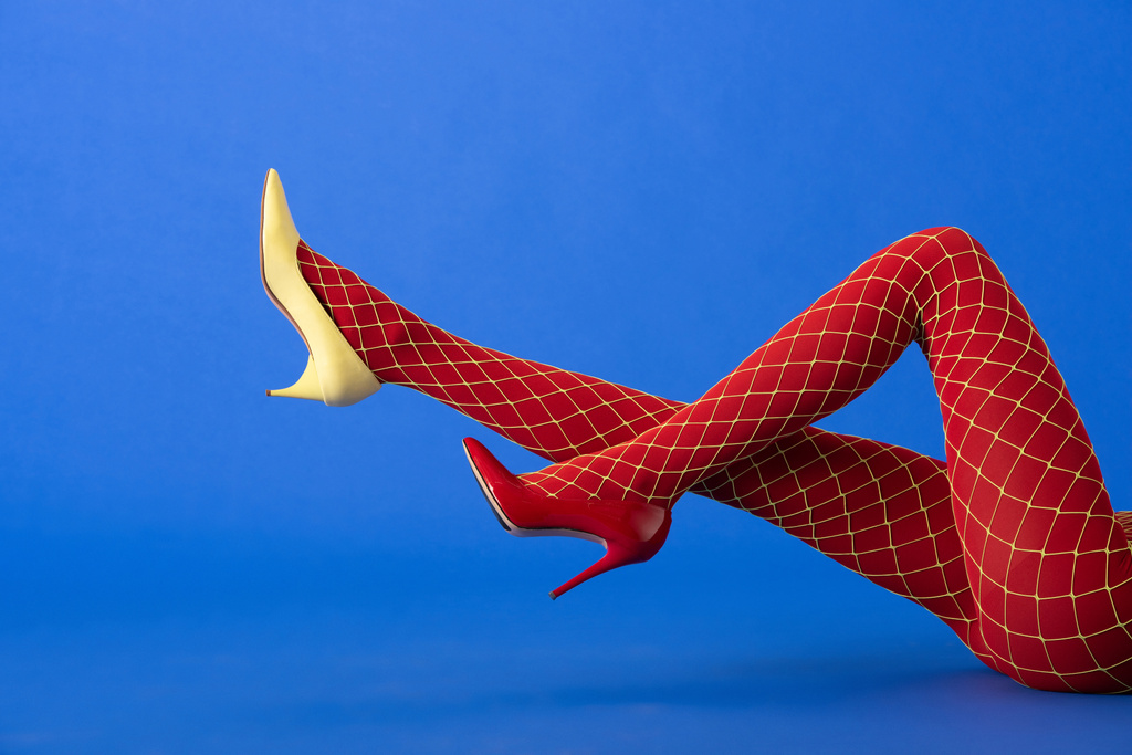 обрезанный вид модели в рыбных сетках колготки, желтые и красные каблуки, лежащие на синем
 - Фото, изображение