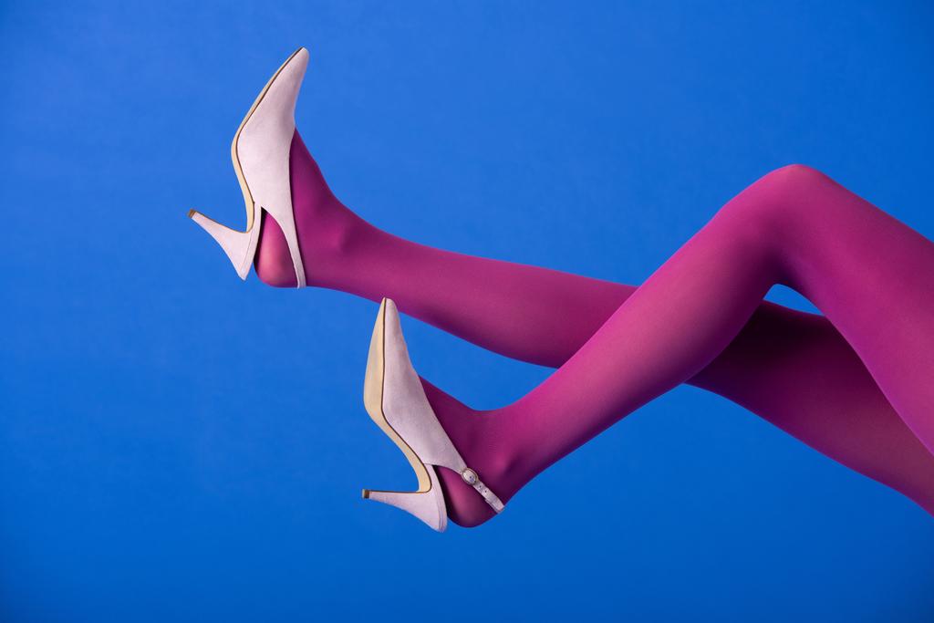 ořezaný pohled na model v jasně fialových punčocháčích a podpatcích pózujících na modré - Fotografie, Obrázek