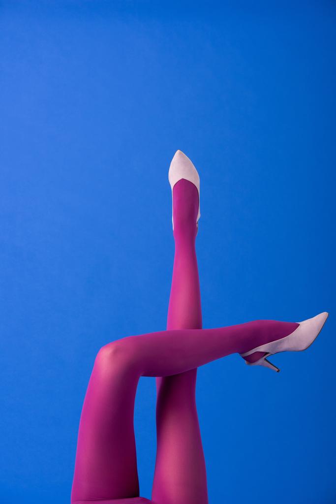 Ausgeschnittene Ansicht einer Frau in lila Strumpfhosen und Schuhen, die auf blau posiert - Foto, Bild