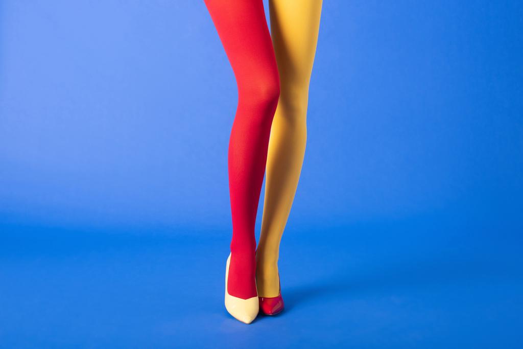 обрізаний вид моделі в жовтих і червоних колготках і взутті, що стоїть на синьому
 - Фото, зображення