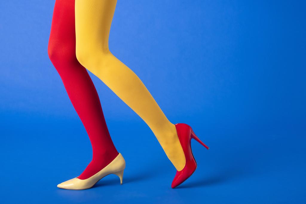 обрезанный вид модели в желтых и красных колготках и обуви, позирующих на синем
 - Фото, изображение