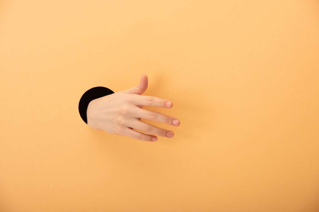 oříznutý pohled na díru s rukou ženy gestikulující na oranžové  - Fotografie, Obrázek