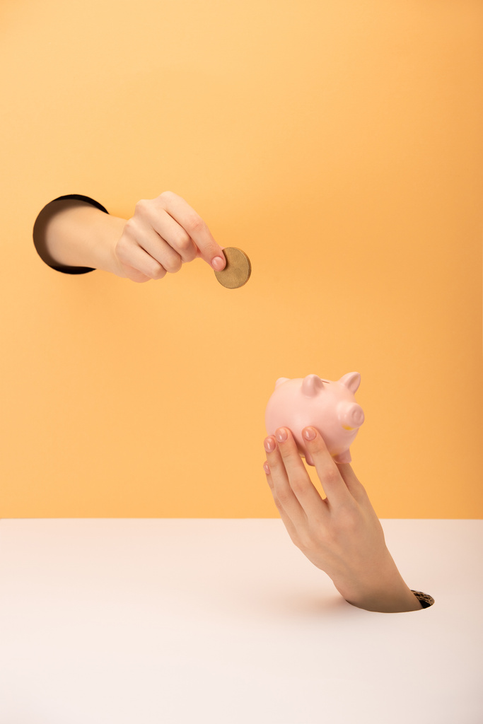 cropped view of woman holding piggy bank and coin on orange and white  - Photo, Image