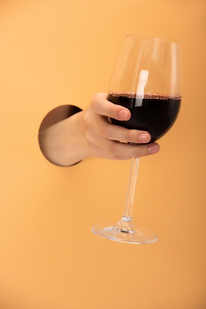 オレンジに赤ワインのワイングラスを持つ女性のクロップドビュー  - 写真・画像