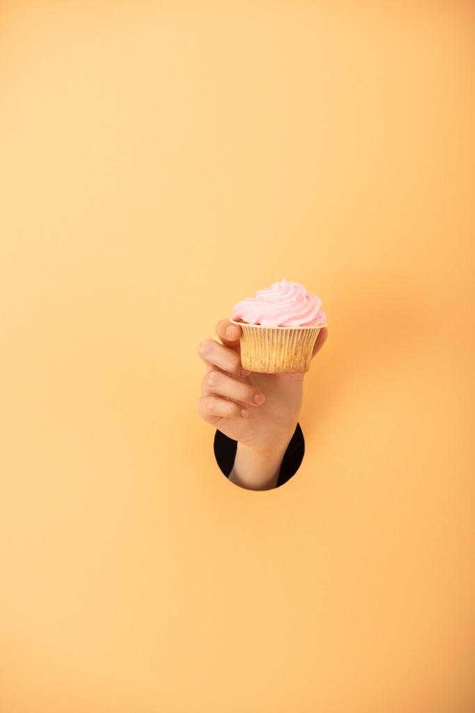 καλλιεργημένη άποψη της γυναίκας που κρατά γλυκό cupcake σε πορτοκαλί - Φωτογραφία, εικόνα
