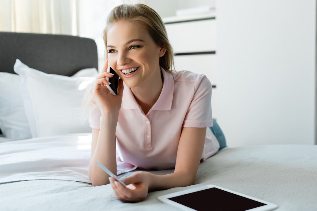 szczęśliwa kobieta rozmawiając na smartfonie i trzymając kartę kredytową w pobliżu tabletu cyfrowego z pustym ekranem w sypialni  - Zdjęcie, obraz