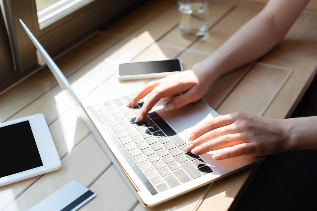 cropped view of woman typing on laptop keyboard near credit card and gadgets with blank screen - Photo, Image