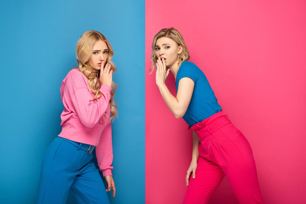 Πλευρική άποψη των ξανθών κοριτσιών που δείχνουν ήσυχο σημάδι σε ροζ και μπλε φόντο - Φωτογραφία, εικόνα