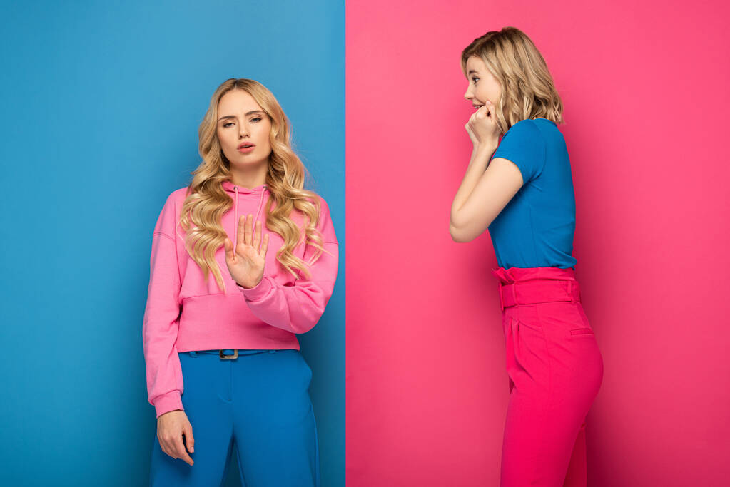 Skeptisches blondes Mädchen zeigt Stoppschild neben überraschter Schwester auf rosa und blauem Hintergrund - Foto, Bild