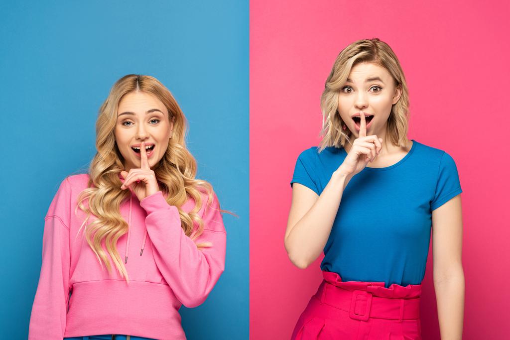 Aufgeregte blonde Schwestern zeigen Schweigezeichen vor der Kamera auf rosa und blauem Hintergrund - Foto, Bild