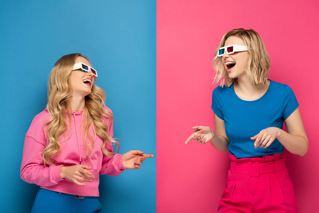 Śmiejące się blondynki w okularach 3D wskazujących palcami na niebieskim i różowym tle - Zdjęcie, obraz