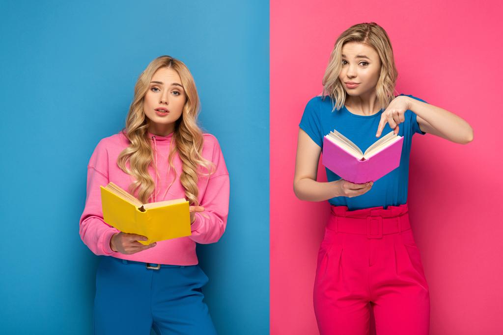 Zdezorientowane blondynki patrzące w kamerę trzymające książki na niebieskim i różowym tle - Zdjęcie, obraz