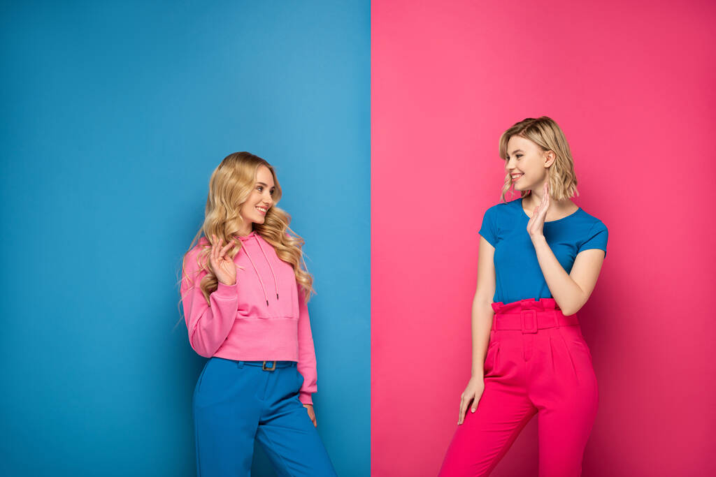 Sorridenti ragazze bionde che si agitano le mani su sfondo rosa e blu
 - Foto, immagini