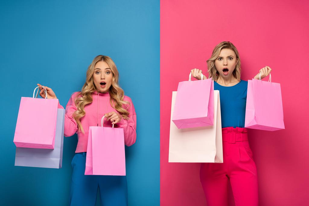 Zaskoczona blondynka siostry z torbami na zakupy patrząc na aparat fotograficzny na różowym i niebieskim tle - Zdjęcie, obraz