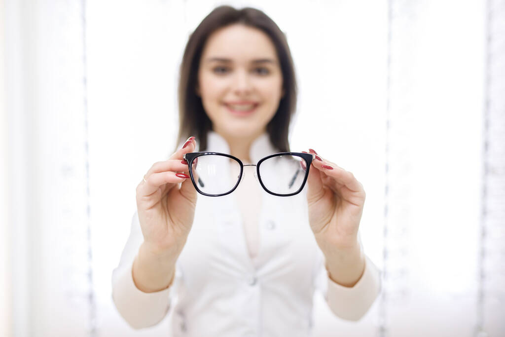 Κοντινές φωτογραφίες, οπτικός νεαρή γυναίκα οπτομέτρης στο κατάστημα οπτικών που κοιτάζει γυαλιά. - Φωτογραφία, εικόνα