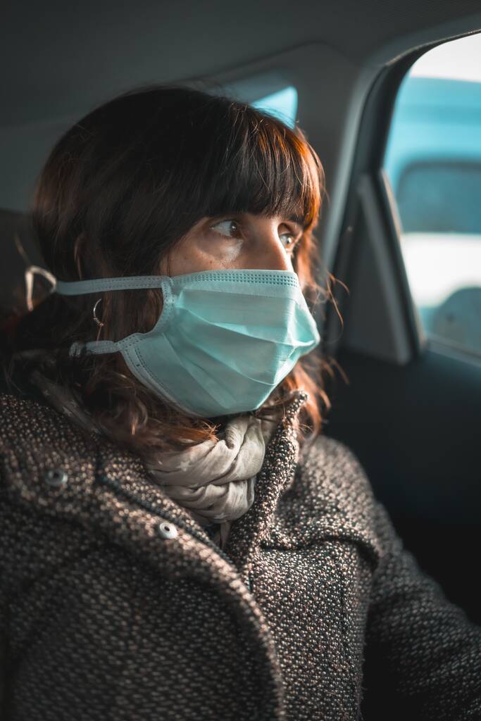 Μια κάθετη φωτογραφία μιας γυναίκας με μια ιατρική μάσκα στο αυτοκίνητο κατά τη διάρκεια της περιόδου καραντίνας - Φωτογραφία, εικόνα