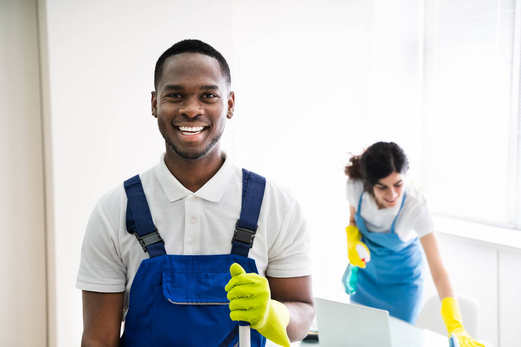 Retrato de um homem feliz zelador com equipamento de limpeza no escritório
 - Foto, Imagem