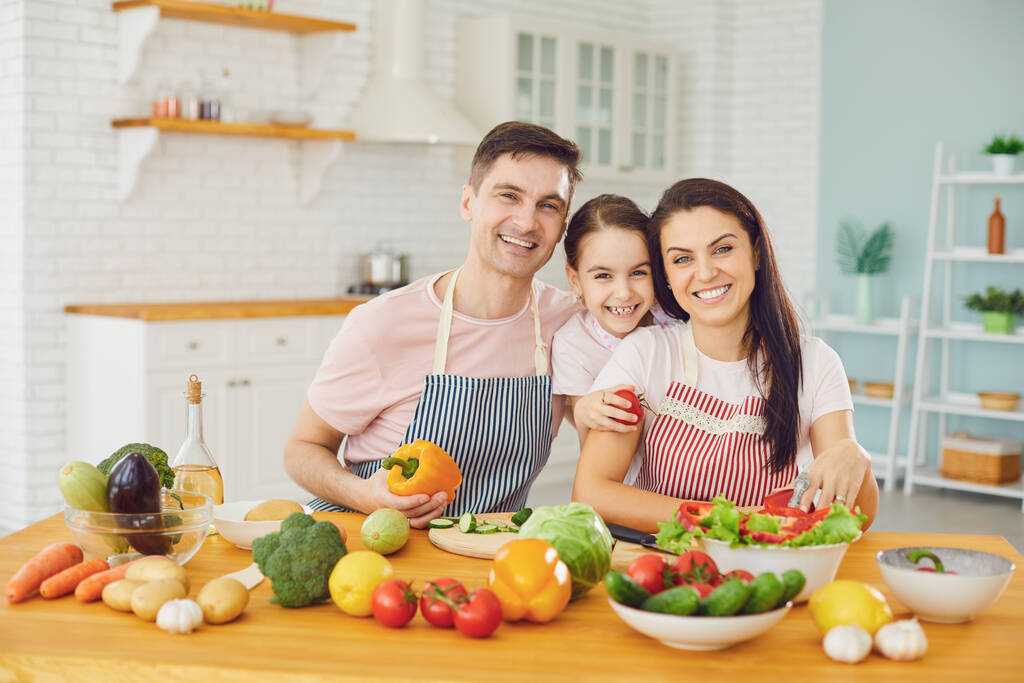 Šťastná rodina s dcerou v kuchyni se zeleninou pohled do kamery. - Fotografie, Obrázek