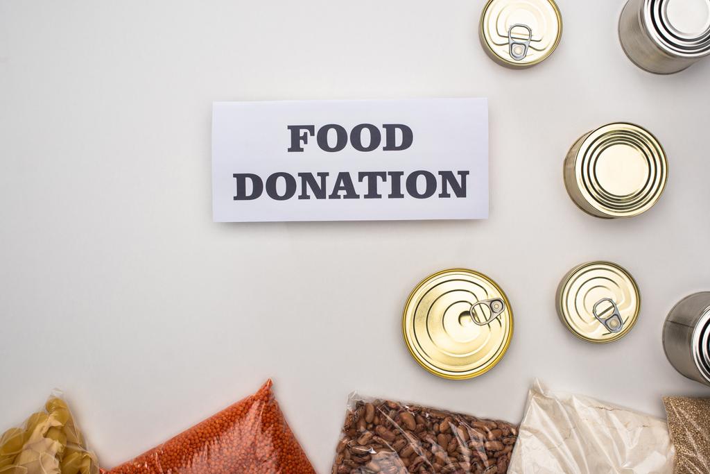 vista superior de latas e grumos em sacos de zíper perto do cartão com letras de doação de alimentos no fundo branco
 - Foto, Imagem